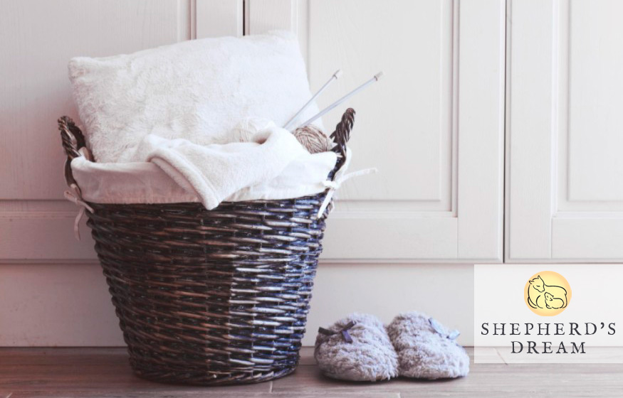 laundry basket sitting on floor, full of wool bedding, with pair of wool slippers sitting next to it